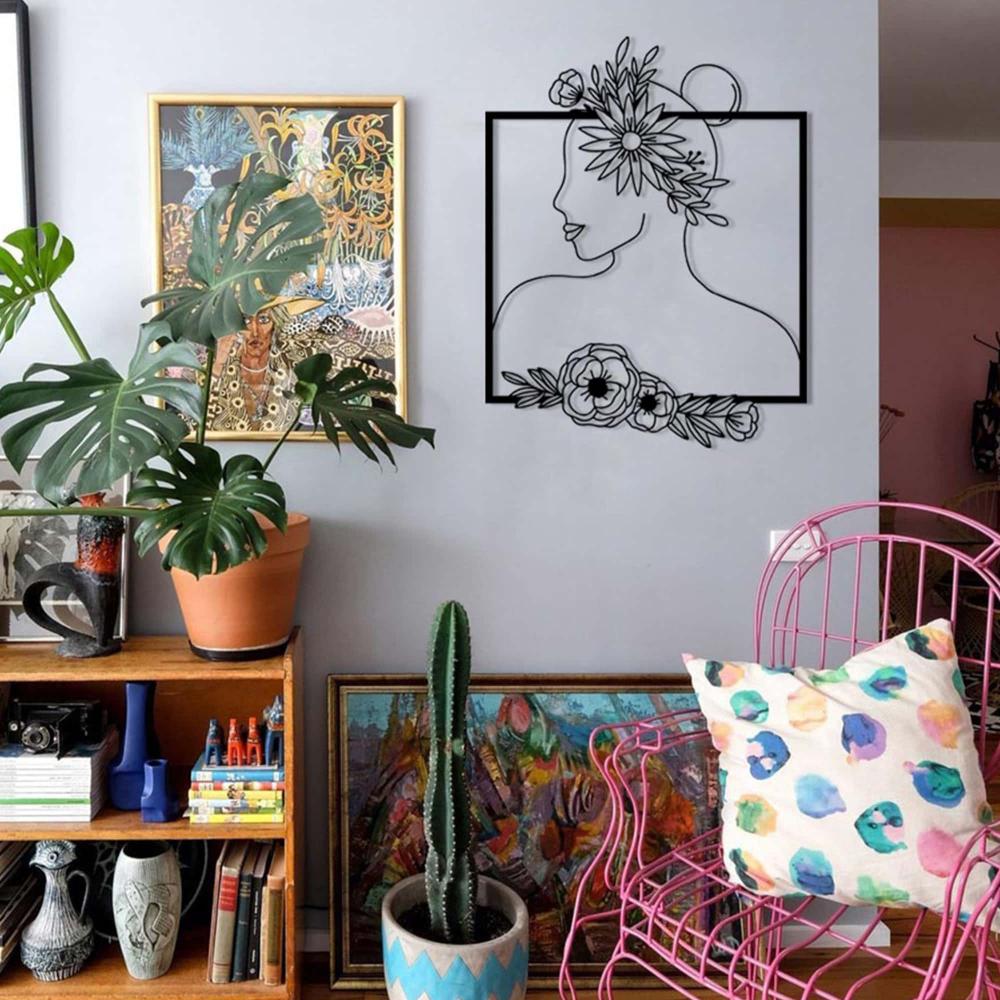 Black floral silhouette wall art featuring a woman's profile with flower accents, displayed in a vibrant room with eclectic decor, a pink chair, and potted plants.
