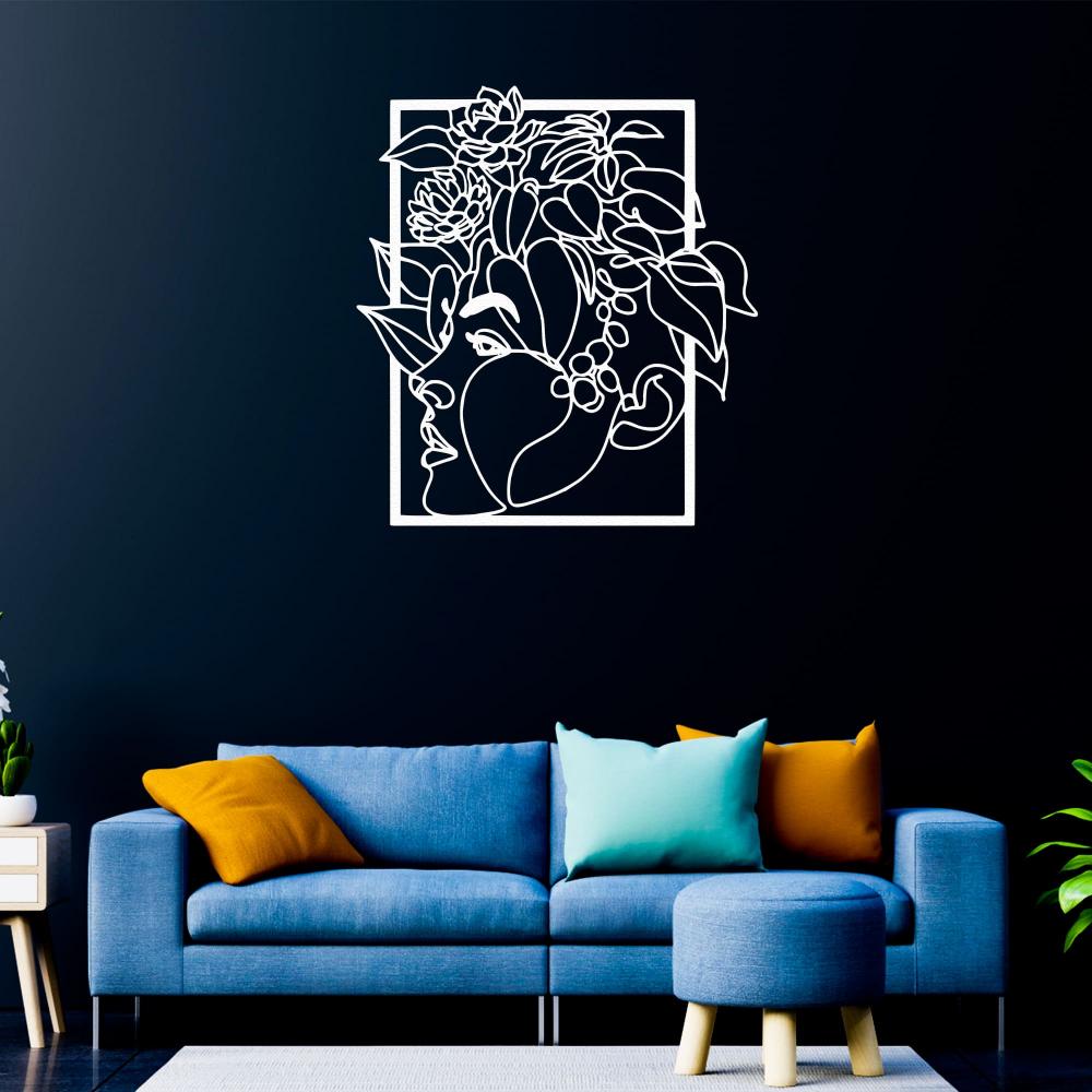 hite metal wall art of a woman's face with floral designs, mounted on a navy blue wall in a cozy living room with colorful cushions on a blue sofa.