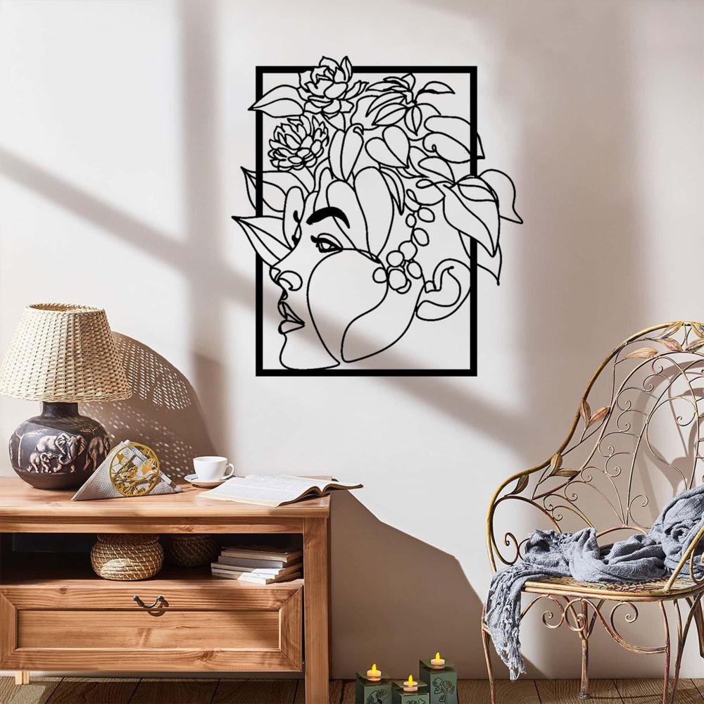 A stylish metal wall art piece of a woman’s face with floral details, mounted above a wooden side table in a naturally lit room with rustic decor.