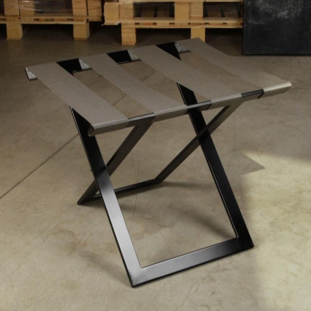 A stylish foldable luggage rack with a metal frame and gray straps, photographed in a warehouse setting to emphasize durability.
