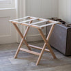 A stylish wooden folding luggage rack placed near a vintage suitcase in a bright and cozy room.