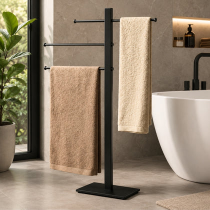 Black freestanding 3-bar towel stand holding towels beside a bathtub in a modern bathroom.