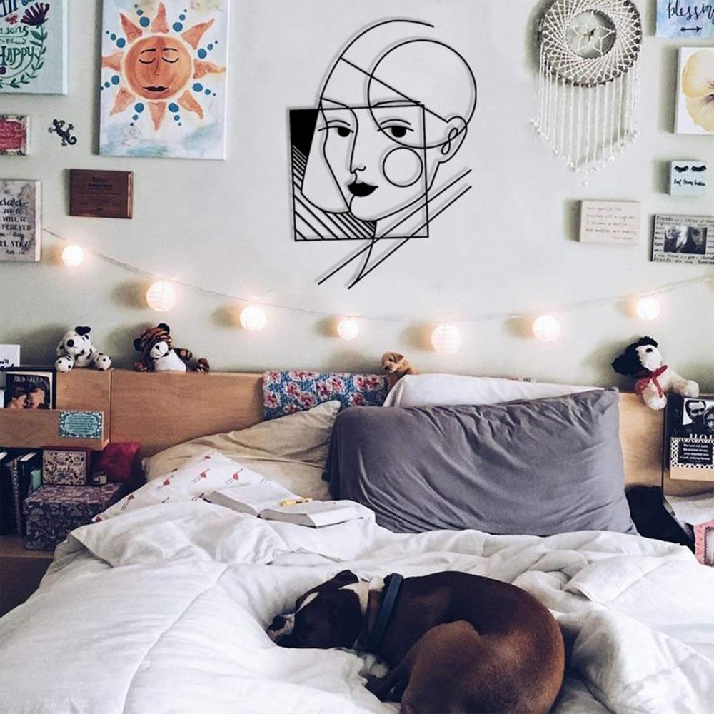 A geometric lady wall art piece mounted above a cozy bed adorned with string lights, surrounded by artistic decor and a dog sleeping on the bed.