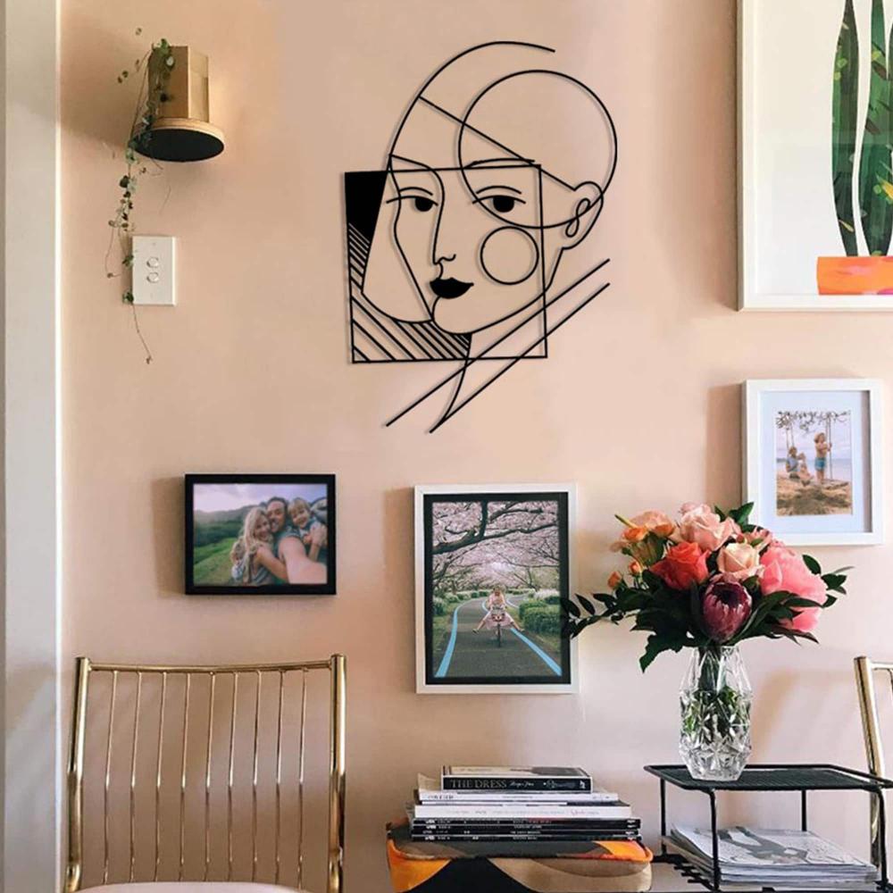 A geometric lady wall art placed on a modern wall surrounded by framed pictures and a vase with fresh flowers on a console.