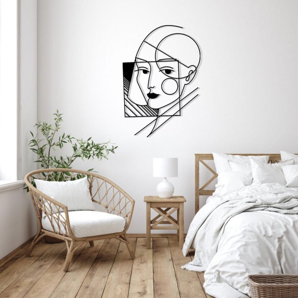 A geometric lady wall art design displayed on a white wall above a minimalistic wooden chair and a bedside table with a lamp.