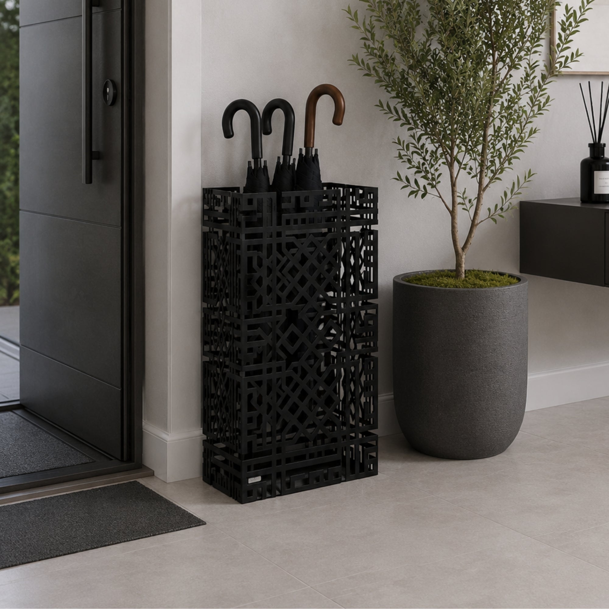Black geometric lattice metal umbrella stand in modern entryway with olive plant and console table