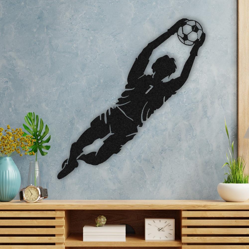 A decorative setting with black metal wall art of a goalkeeper catching a soccer ball, mounted on a light blue textured wall above a wooden console with decor items.