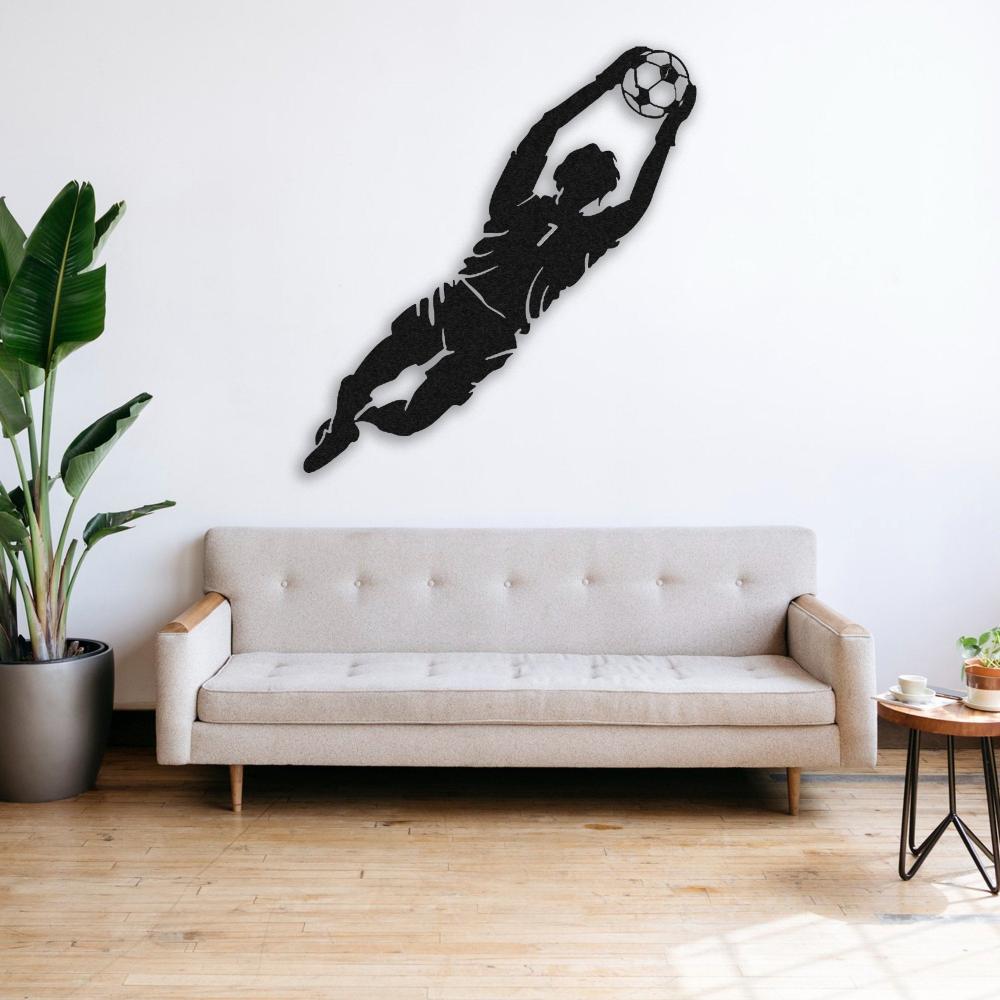 A minimalist living room featuring black metal wall art of a goalkeeper diving to catch a soccer ball, mounted above a light beige sofa next to a green plant.