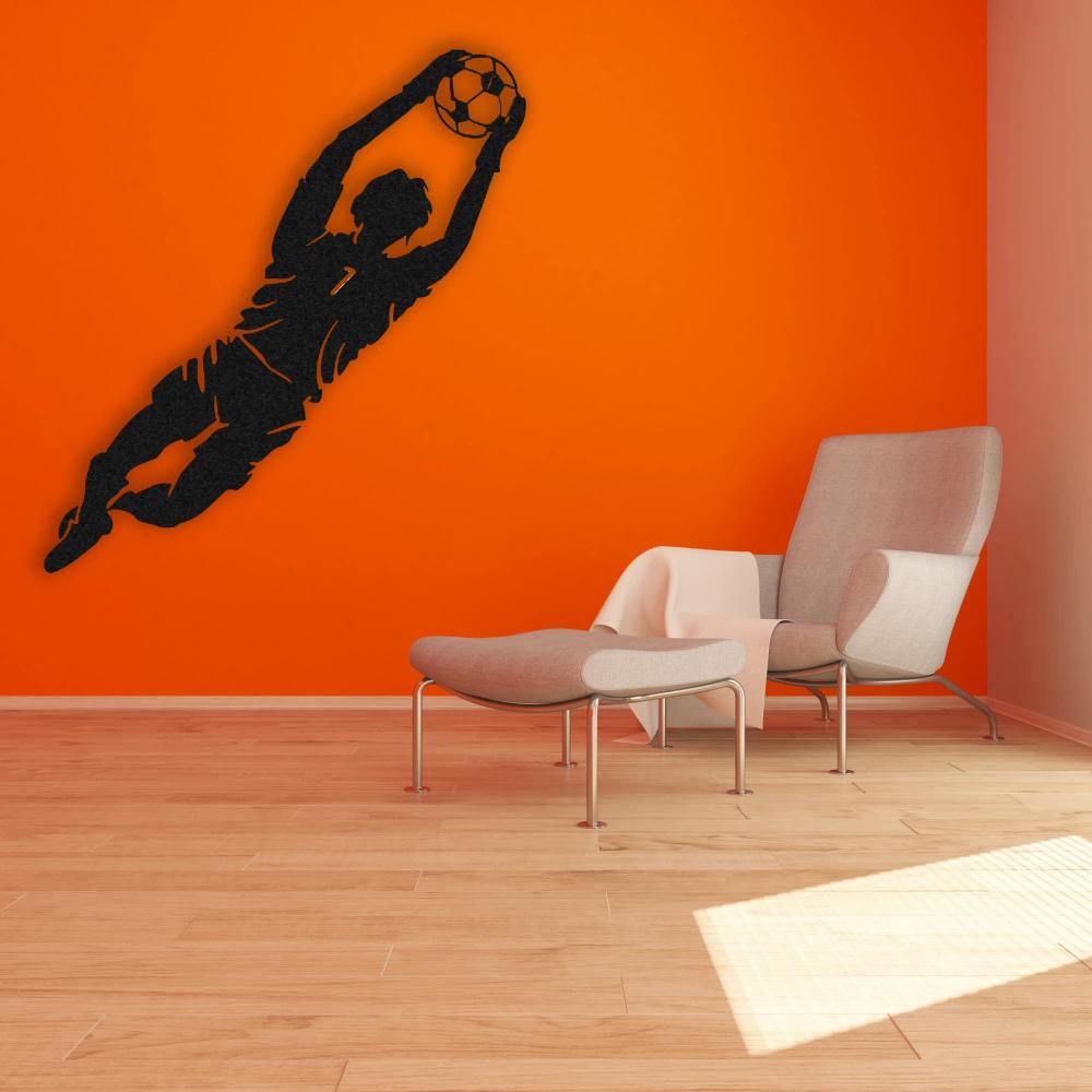A vibrant interior with black metal wall art of a goalkeeper leaping to save a soccer ball, mounted on an orange wall beside a modern armchair and ottoman.