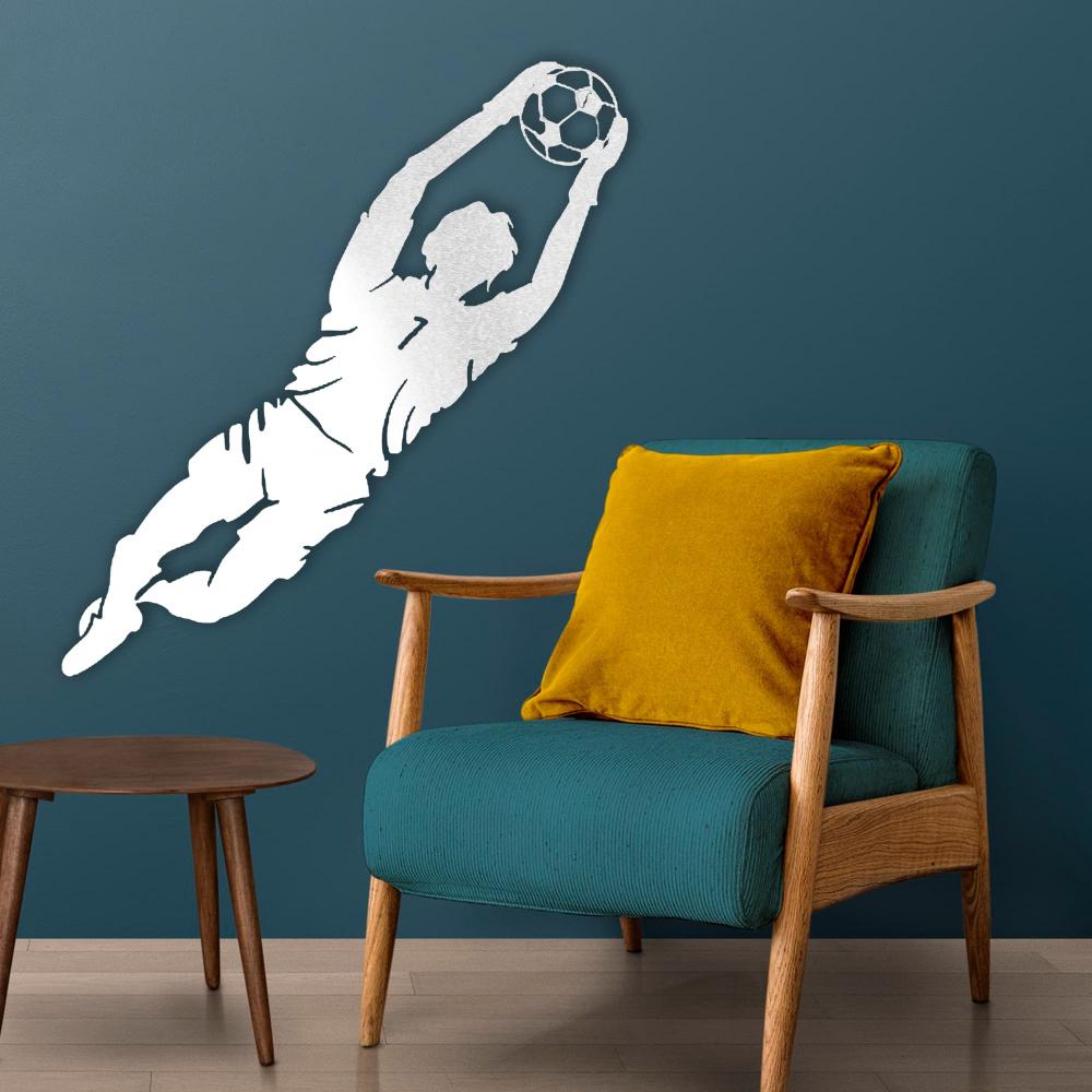 modern room with white metal wall art depicting a goalkeeper diving to catch a soccer ball, mounted on a teal wall above a blue armchair with a yellow cushion.