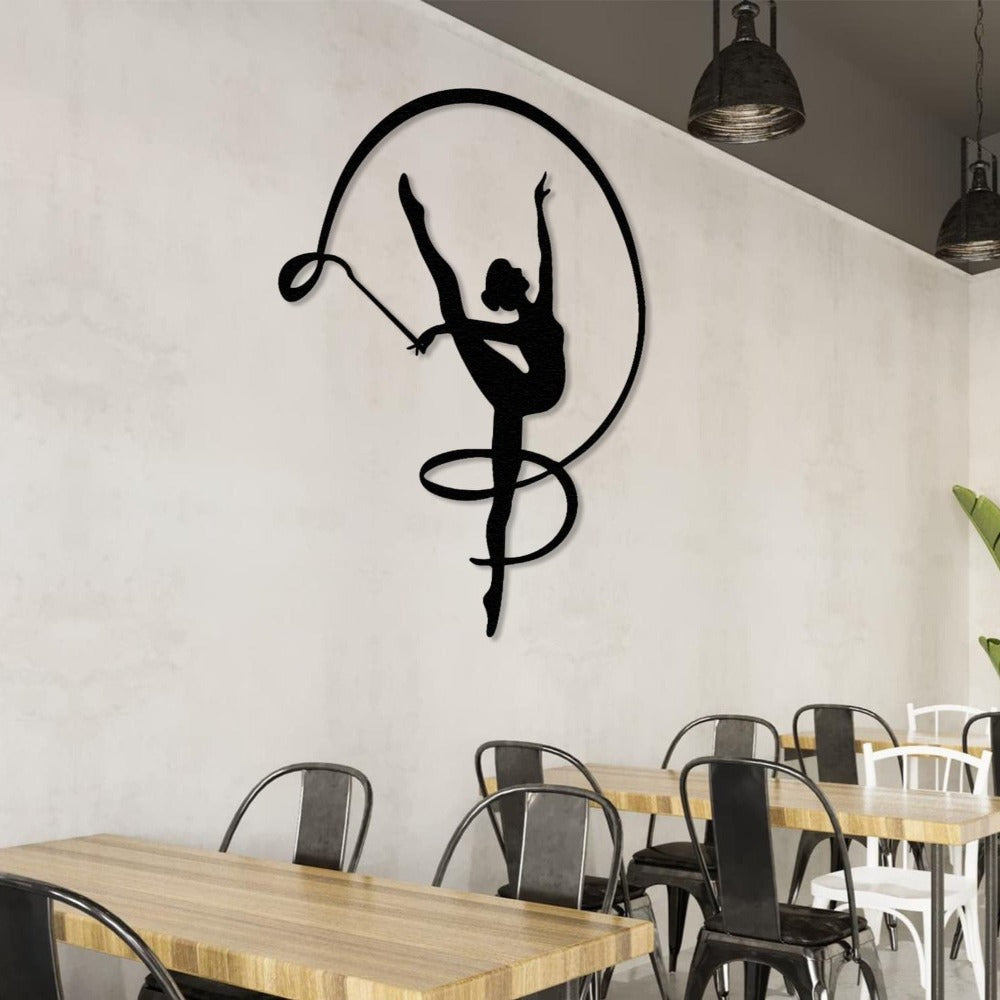 A contemporary cafe setting with gymnast girl metal wall decor in black, depicting a rhythmic ribbon dance silhouette, mounted on a plain white wall surrounded by industrial-style seating.