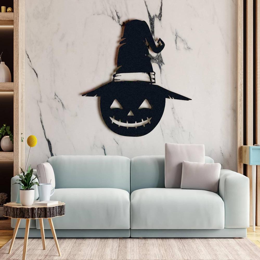 Black jack-o'-lantern metal wall decor with a witch's hat, displayed on a wall with a light marble background above a pastel blue sofa.