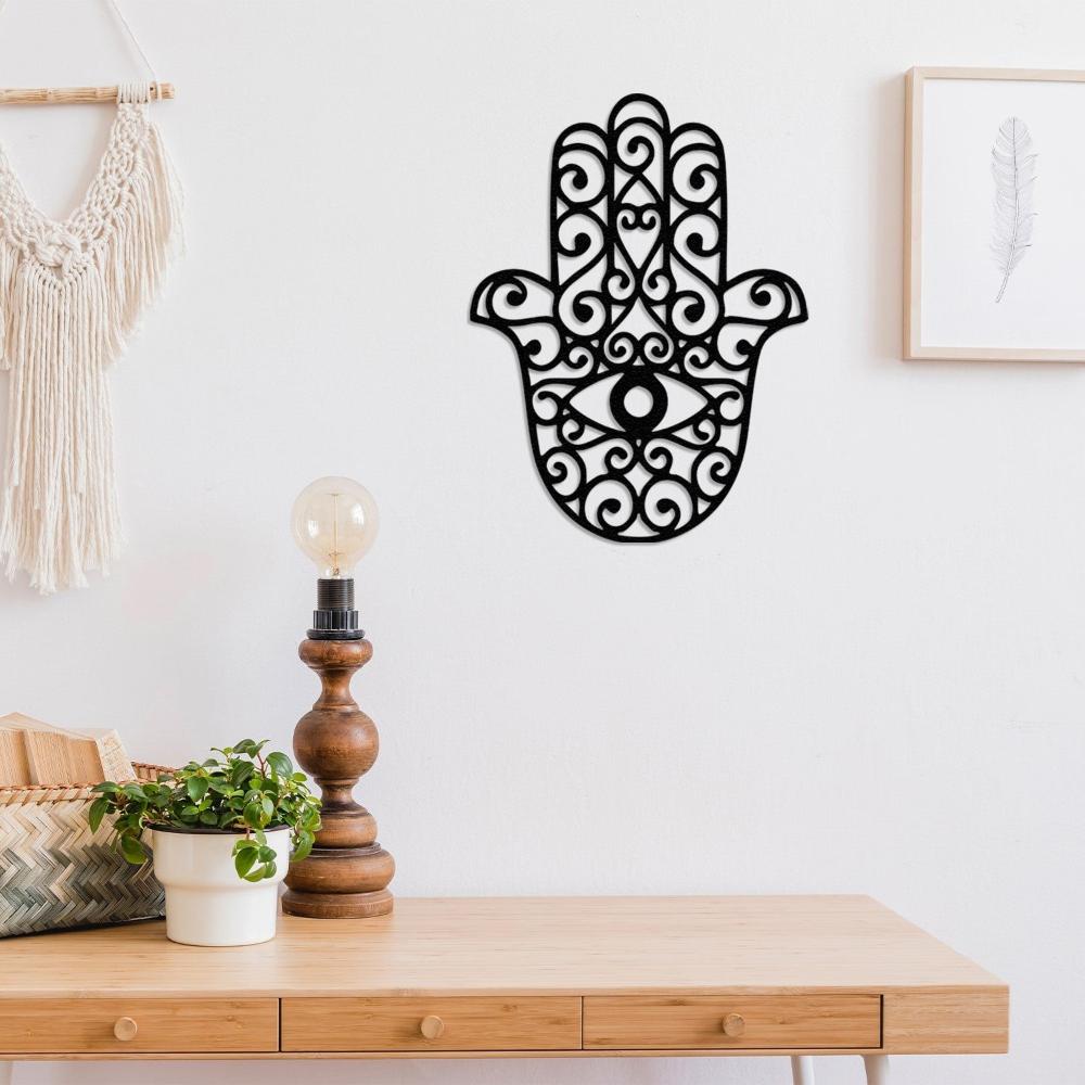 A stylish Hamsa hand metal wall decor with intricate patterns and an eye symbol, displayed above a wooden desk with a boho-style lamp and plants.