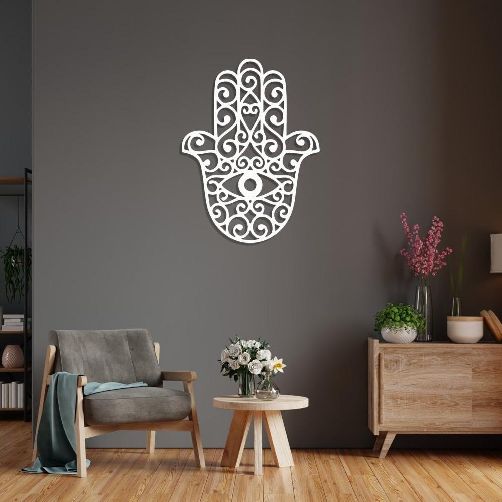A white Hamsa hand metal wall art featuring a modern eye design, displayed in a living room with a comfortable chair, a small table, and a vase of flowers.