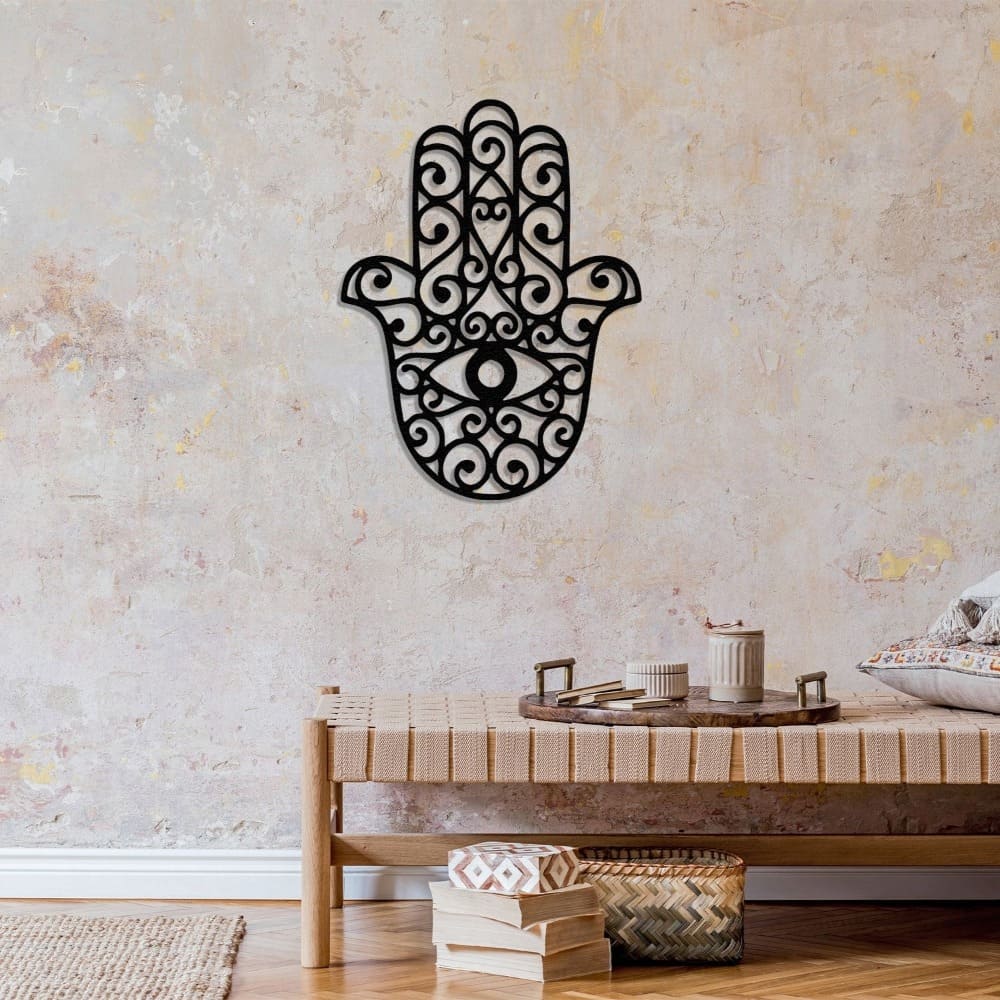 A black Hamsa hand metal wall decor with a textured background, adding a bohemian touch to a cozy space featuring a woven bench and decorative trays.