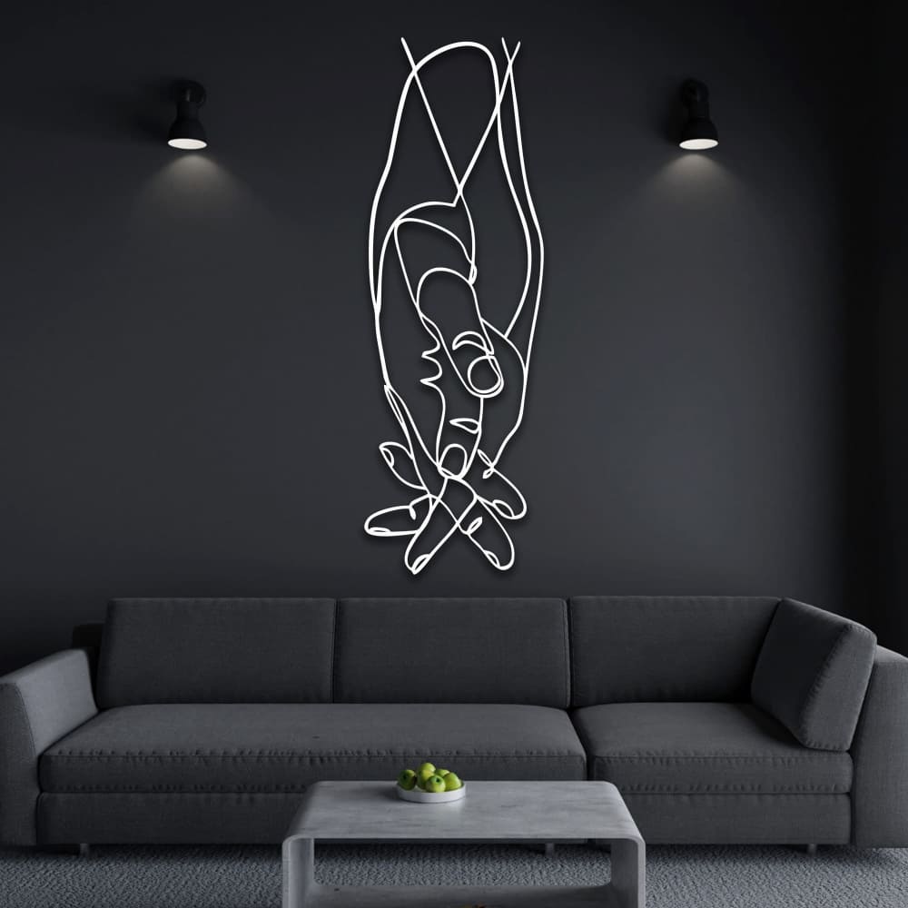White intertwined hands metal wall decor on a dark wall, illuminated by sleek overhead lighting, styled with a gray sofa.