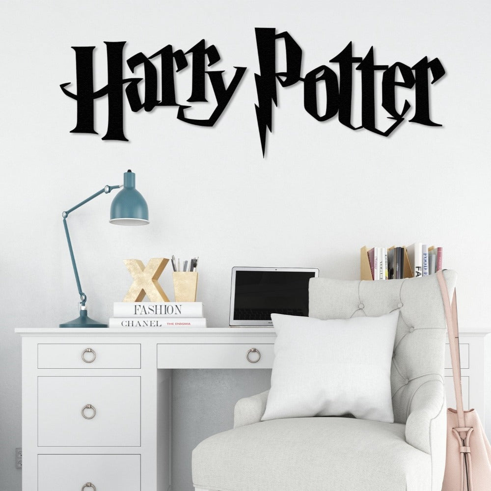 "Harry Potter" black metal wall art featuring a lightning bolt design, displayed on a white wall above a modern white desk with ring pull handles. The desk setup includes a teal desk lamp, gold letter 'X' decor, stacked books, and a laptop, complemented by a tufted light gray chair with a white cushion.