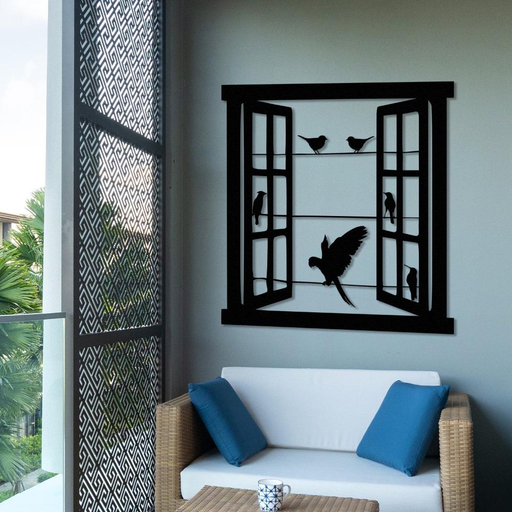 Black metal wall art of an open window with birds perched and a parrot in flight, displayed in a cozy outdoor seating area with a wicker sofa and blue cushions, overlooking greenery.