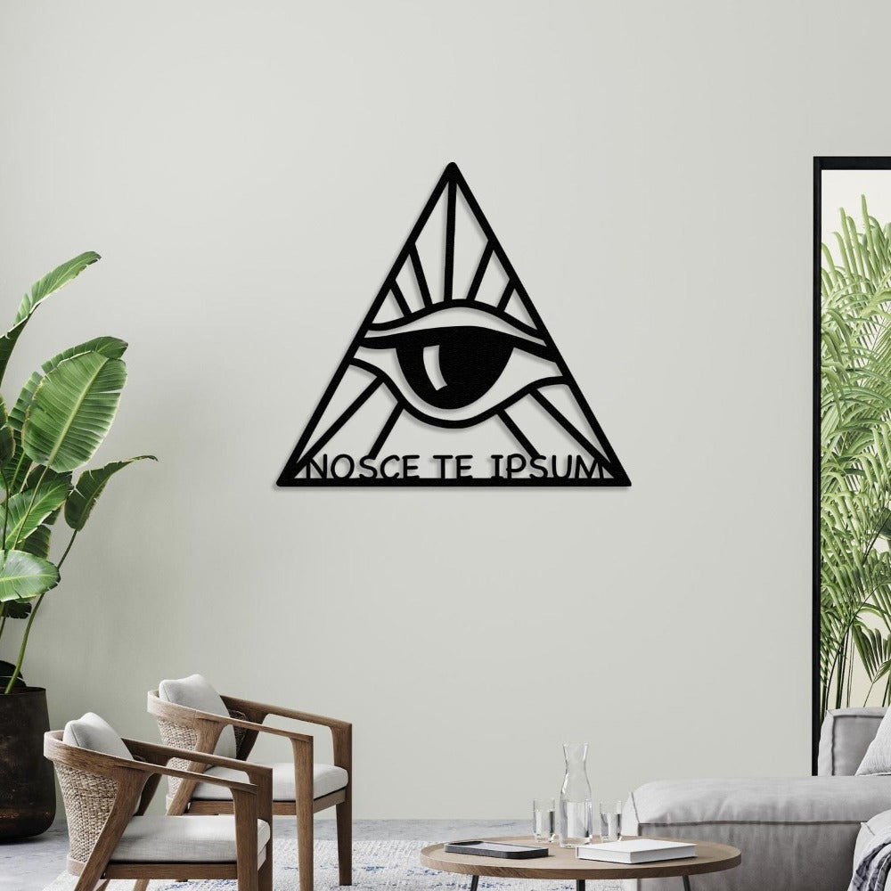 Black triangular metal wall art featuring an eye design and the phrase "Nosce Te Ipsum" (Know Thyself), displayed on a light-colored wall in a modern living room with a wooden coffee table, chairs, and green indoor plants.