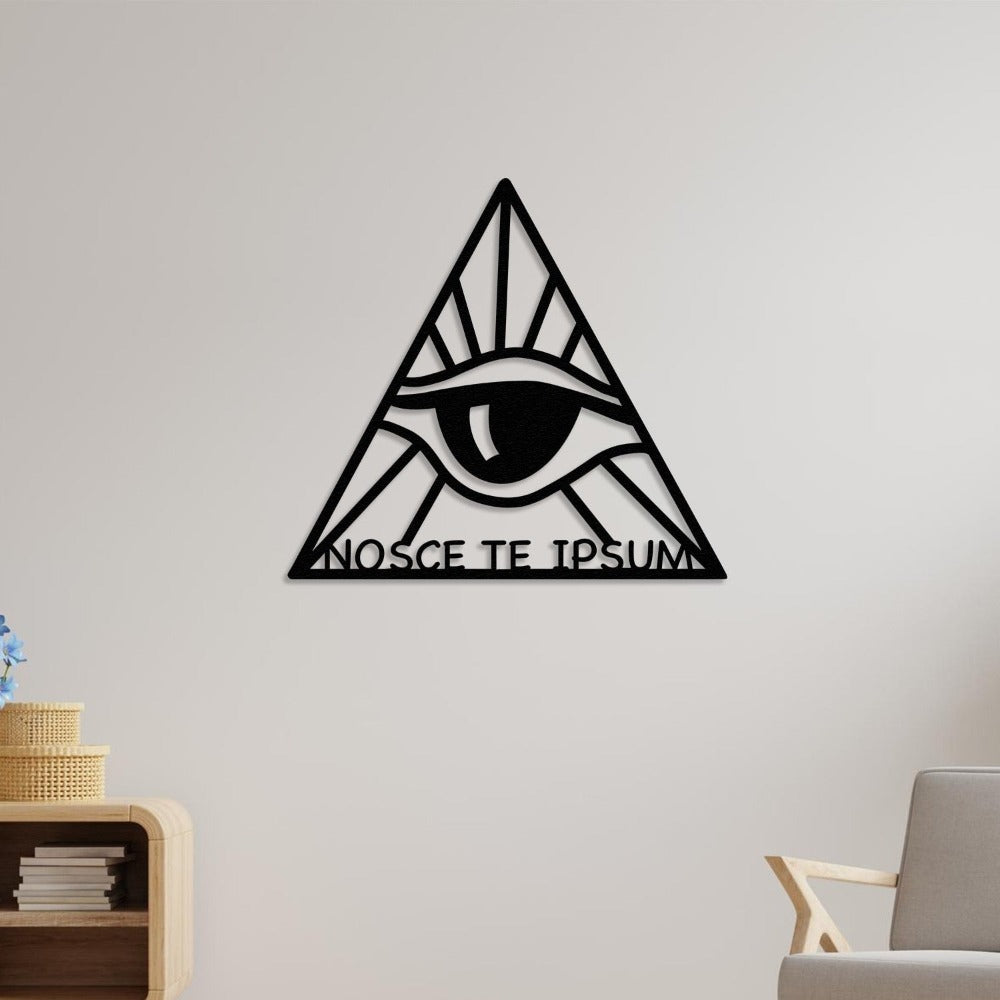 Minimalist room featuring the black "Know Thyself" metal wall art with an eye within a triangle design. The phrase "Nosce Te Ipsum" is elegantly integrated at the bottom of the triangle. Positioned above a modern wooden shelf with stacked books and a decorative basket, next to a contemporary beige chair.