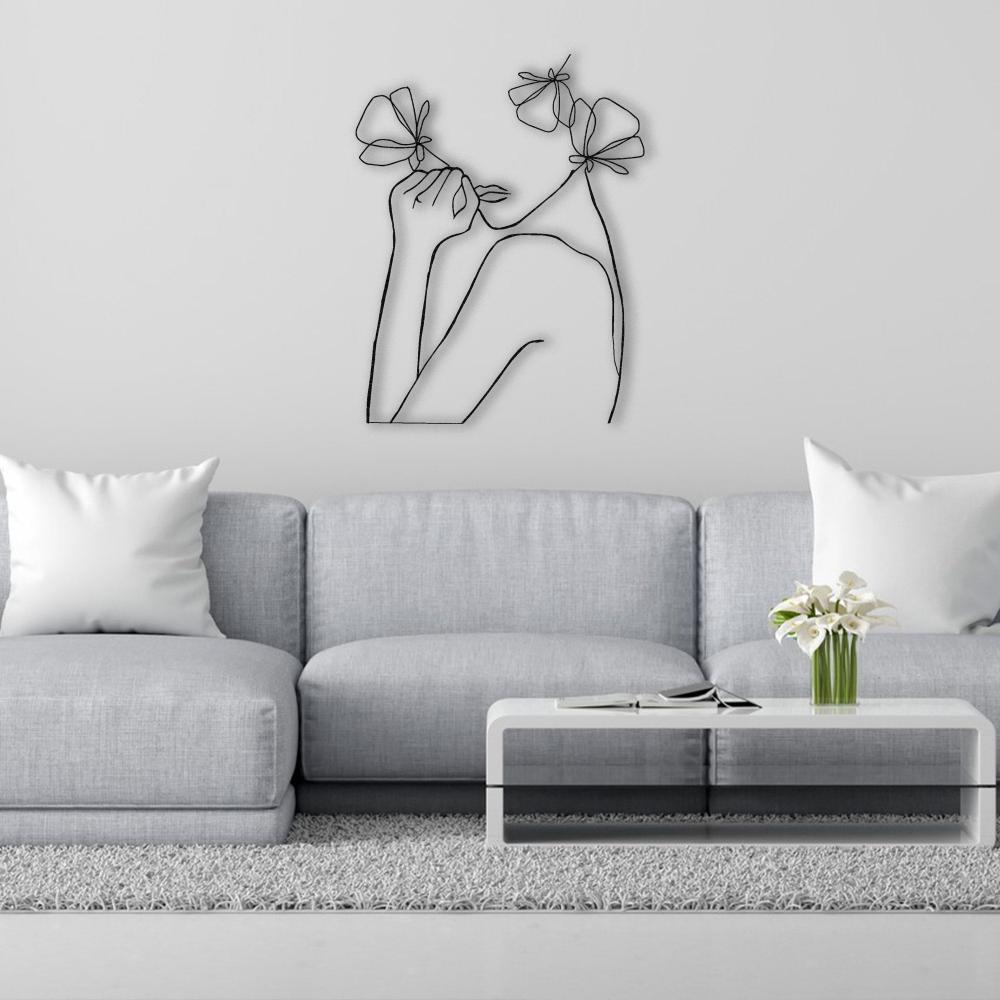 A modern line art wall decor featuring an abstract female figure with flowers, mounted above a light gray couch in a minimalist living room setting.