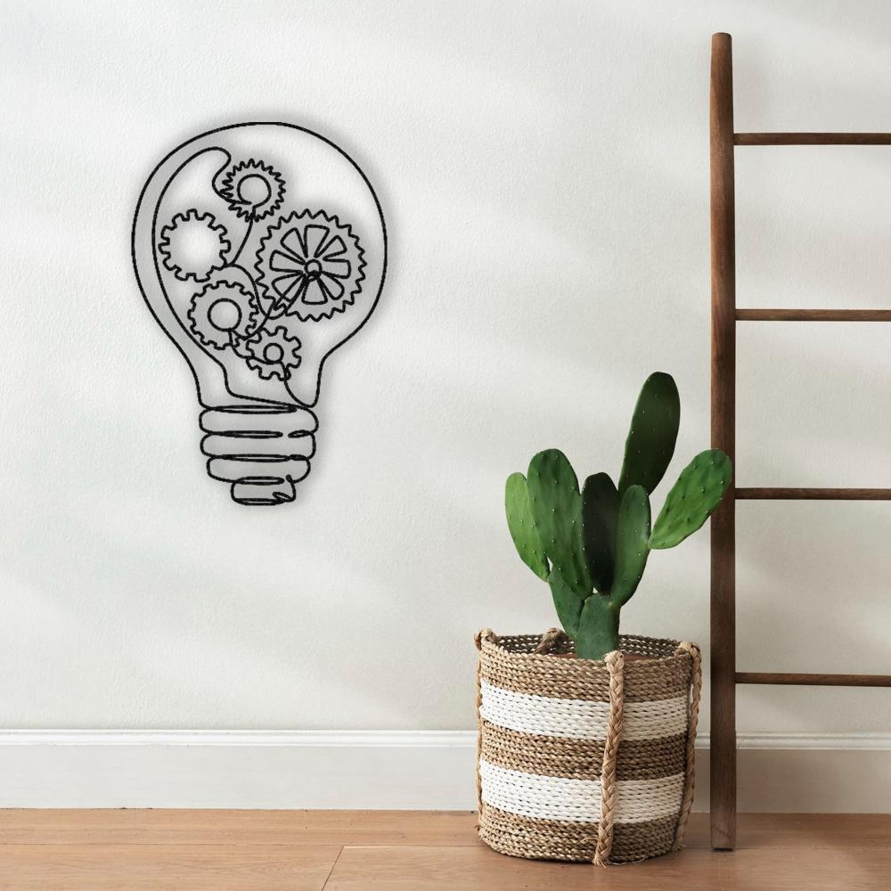 Light bulb-shaped metal wall art with intricate gear designs, displayed on a minimalist wall next to a woven basket containing a cactus and a wooden ladder.