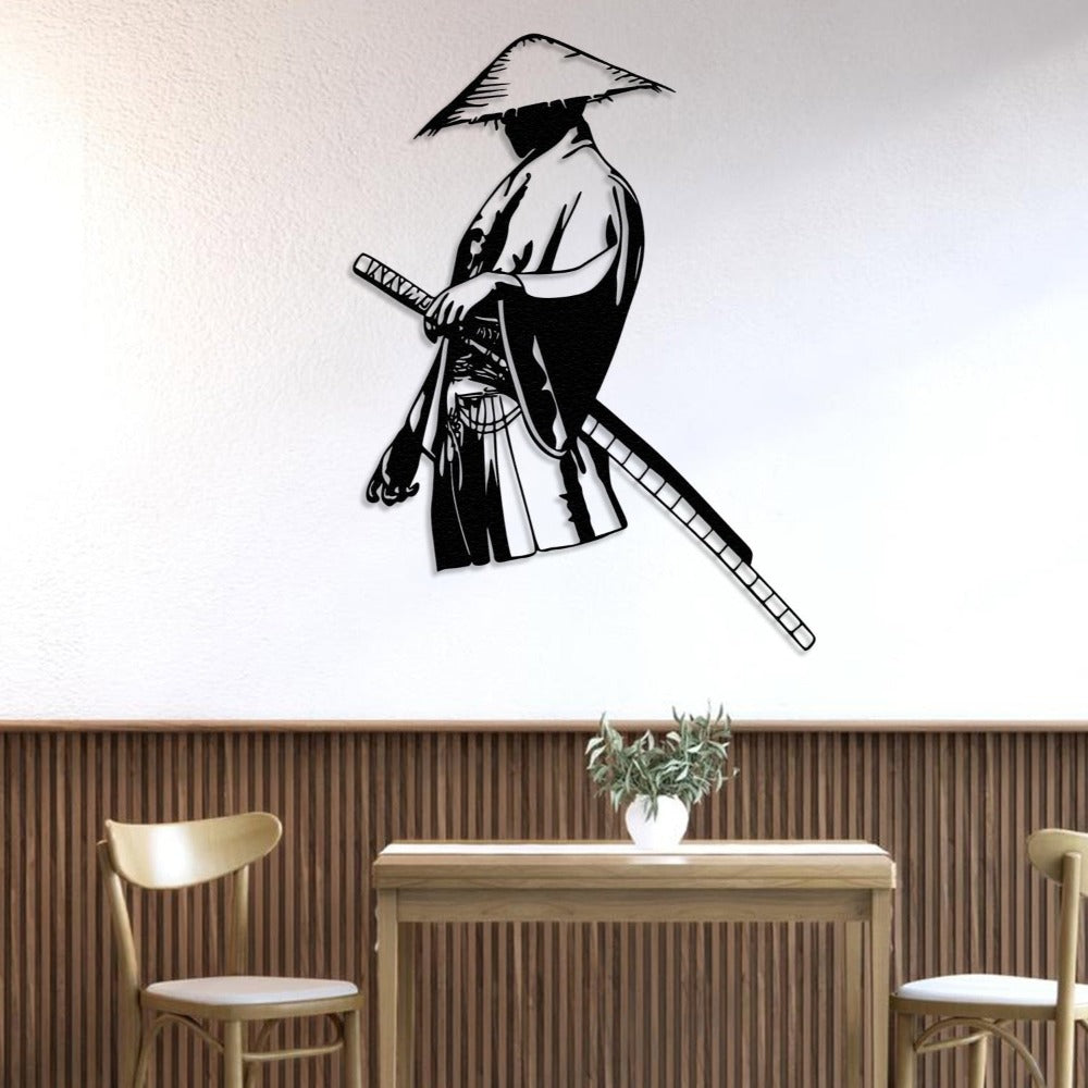 Black metal wall art of a solitary samurai holding a katana, wearing a traditional straw hat, mounted on a white wall above a wooden dining table with a plant centerpiece.