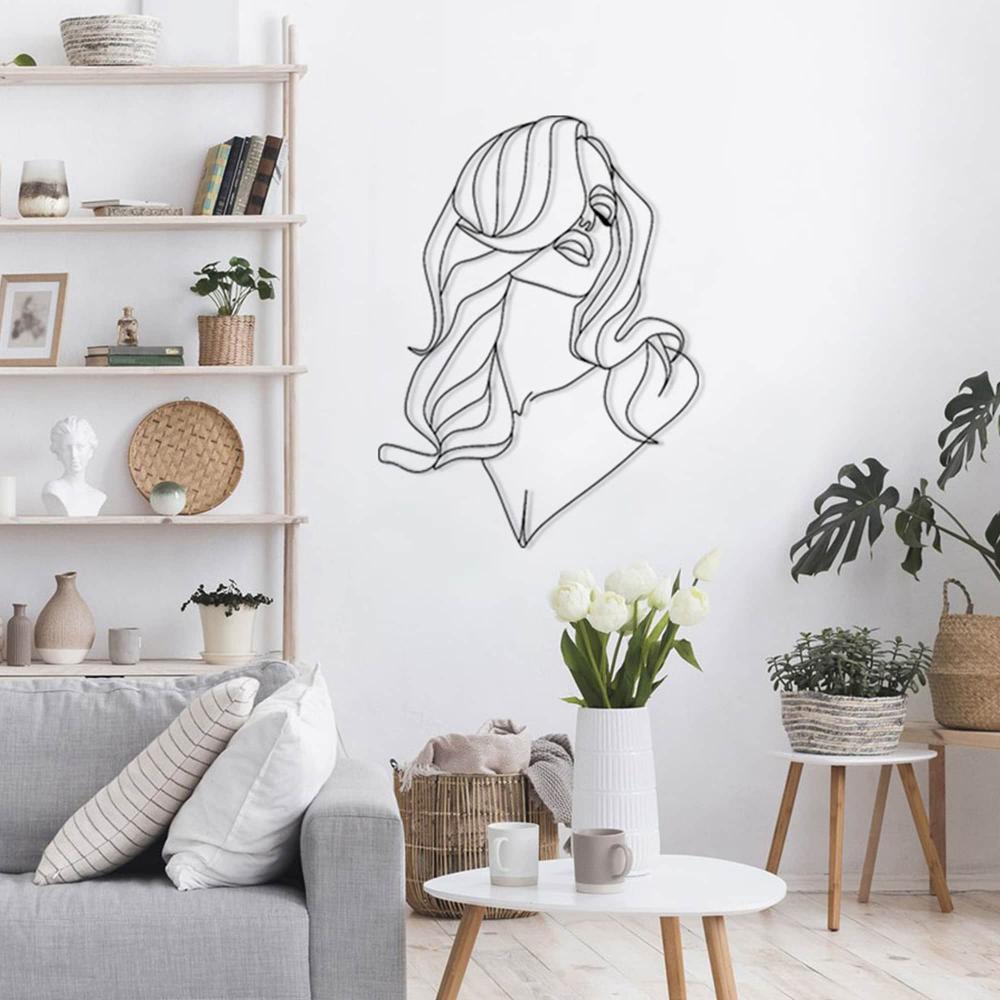 Minimalist metal wall art of a woman's long hair and elegant silhouette, displayed on a white wall in a serene living room. The room features a light gray sofa, wooden furniture, a vase of white tulips, and decorative shelves with books and ornaments.