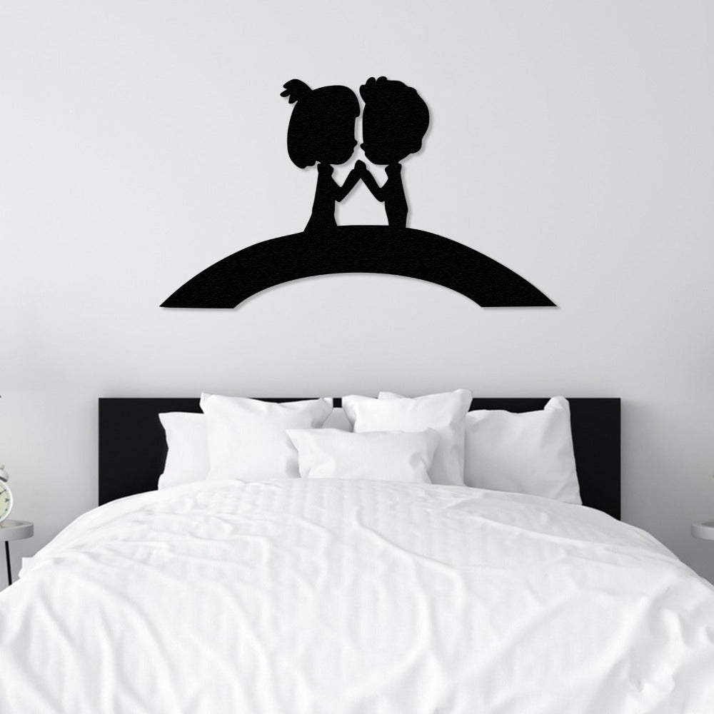 Black metal wall art of a couple on a bridge, placed above a white bed for elegant and romantic bedroom decor.