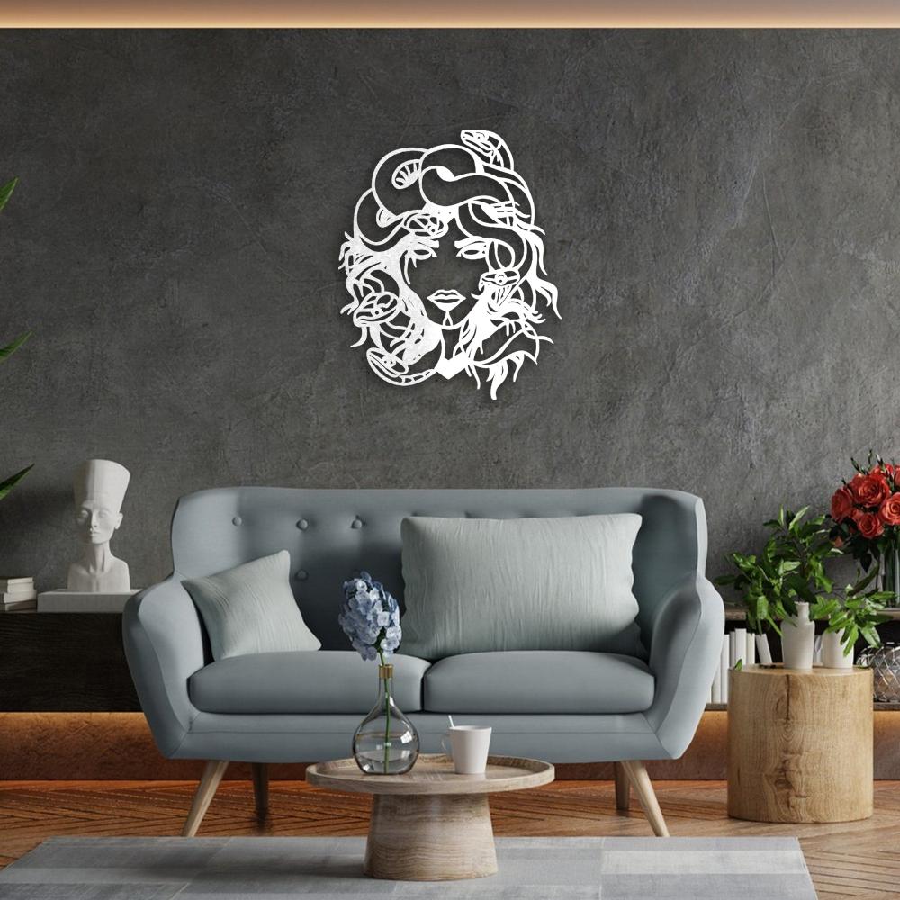 White Medusa metal wall art featuring intricate snake and face details mounted on a textured dark wall above a modern light blue sofa, surrounded by plants and artistic decor elements.