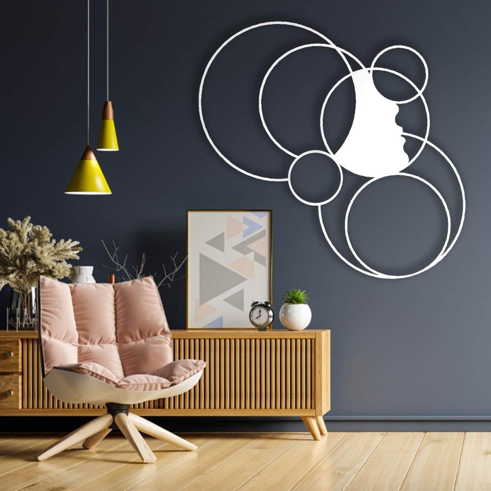 Modern white metal wall art featuring a girl's silhouette surrounded by overlapping circles, mounted on a dark blue wall above a wooden sideboard with decorative items and a cozy armchair in a contemporary living space.
