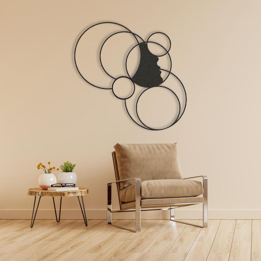 Minimalist metal wall art featuring a girl's silhouette surrounded by interconnected geometric circles, mounted on a beige wall above a modern armchair and wooden side table with decorative plants.