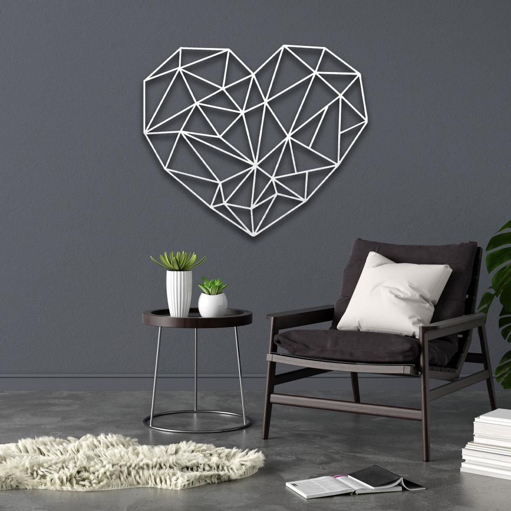 Contemporary geometric heart-shaped metal wall art in elegant white color displayed on a gray wall above a cozy black chair with a white cushion, accompanied by a round side table and decorative plants.
