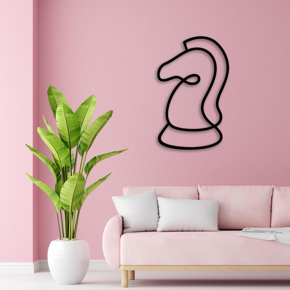 A sleek black chess knight metal wall art on a pink wall, accompanied by a pink sofa and a vibrant green plant.