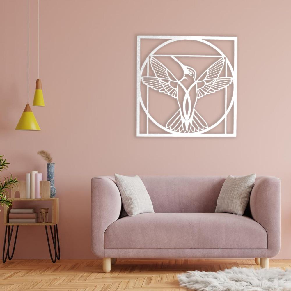 Elegant white metal wall art of a hummingbird with wings spread inside a geometric circular frame, mounted on a pastel pink wall above a modern pink sofa.