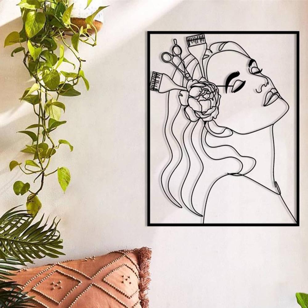 A cozy corner featuring black metal wall art of a woman’s profile adorned with a flower and hairdressing tools, mounted on a light wall next to hanging greenery and a textured pillow.
