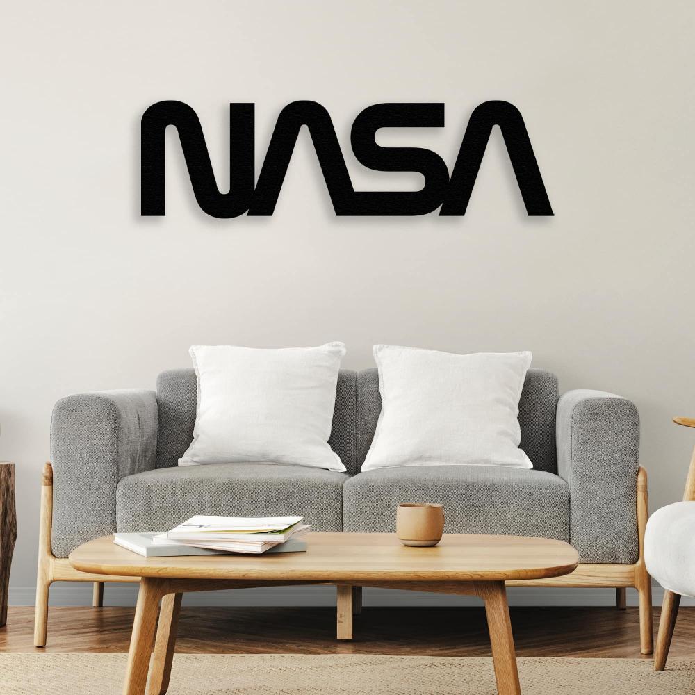 Black NASA metal wall art displayed above a modern gray sofa with white cushions, creating a sleek and futuristic decor style, complemented by a wooden coffee table featuring books and a mug.