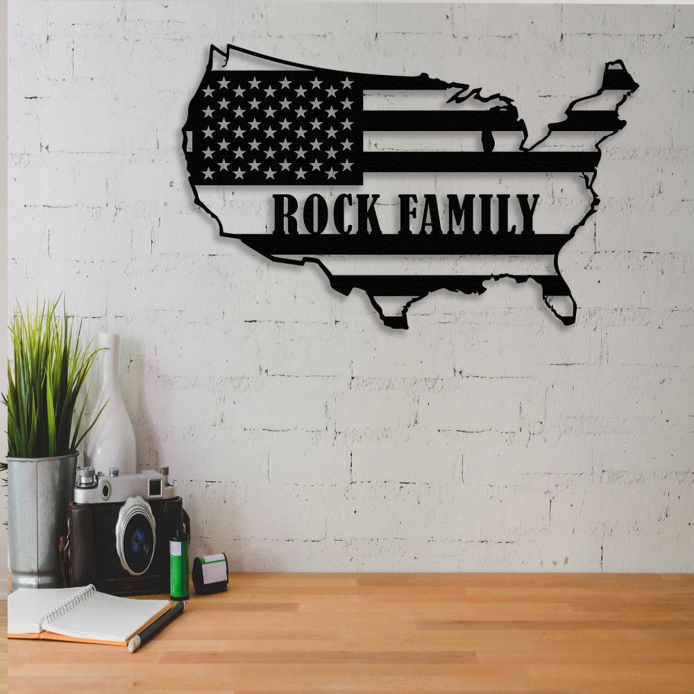 USA map black metal wall art with "Rock Family" text mounted on a white brick wall, paired with a wooden desk and decorative items for a casual workspace.