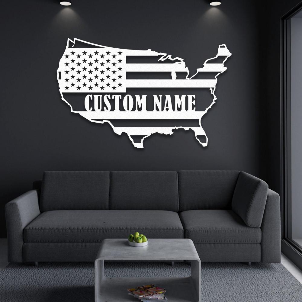 White metal wall art of the USA map with customizable text, displayed on a dark wall above a gray sofa in a sleek modern setting.