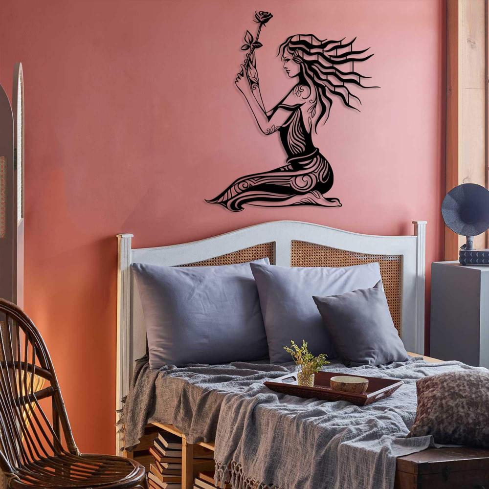 Cozy bedroom featuring a coral pink accent wall adorned with intricate black metal wall art of a woman holding a rose. The room includes a vintage-style rattan headboard, gray bedding with soft throws, and a decorative tray with small plants for a serene, eclectic ambiance.