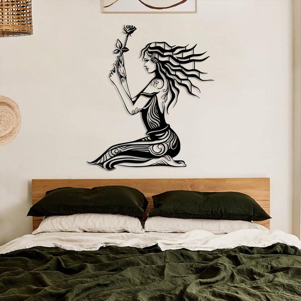 Minimalist bedroom showcasing a black metal wall art of a woman holding a rose, mounted above a wooden bed frame with dark green bedding and crisp white sheets. The decor includes a wicker hanging element and soft natural tones for a cozy, earthy vibe.
