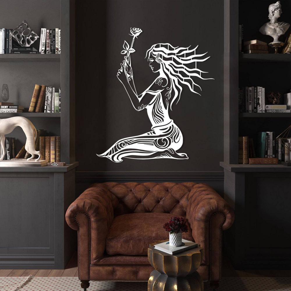 White metal wall art of a seated woman holding a rose, featuring intricate patterns and flowing hair, mounted on a dark wall in a sophisticated library setting. The room includes a classic brown leather armchair, a metallic side table with a flower vase, built-in shelves filled with books, and artistic sculptures for a luxurious and elegant ambiance.