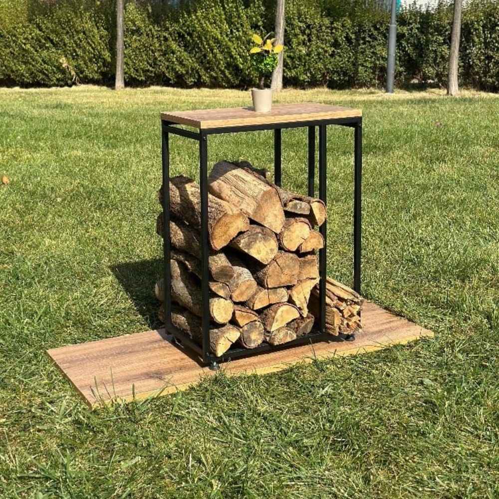 A minimalist black metal log rack with a wooden top, placed outdoors on grass, holding stacked firewood and kindling