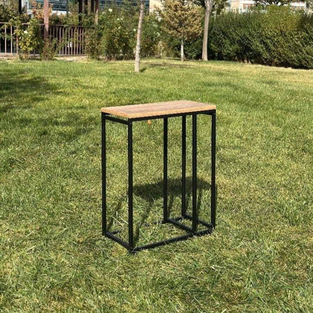 An empty minimalist black metal log rack with a wooden top, displayed outdoors on grass, showing its sleek and modern design.