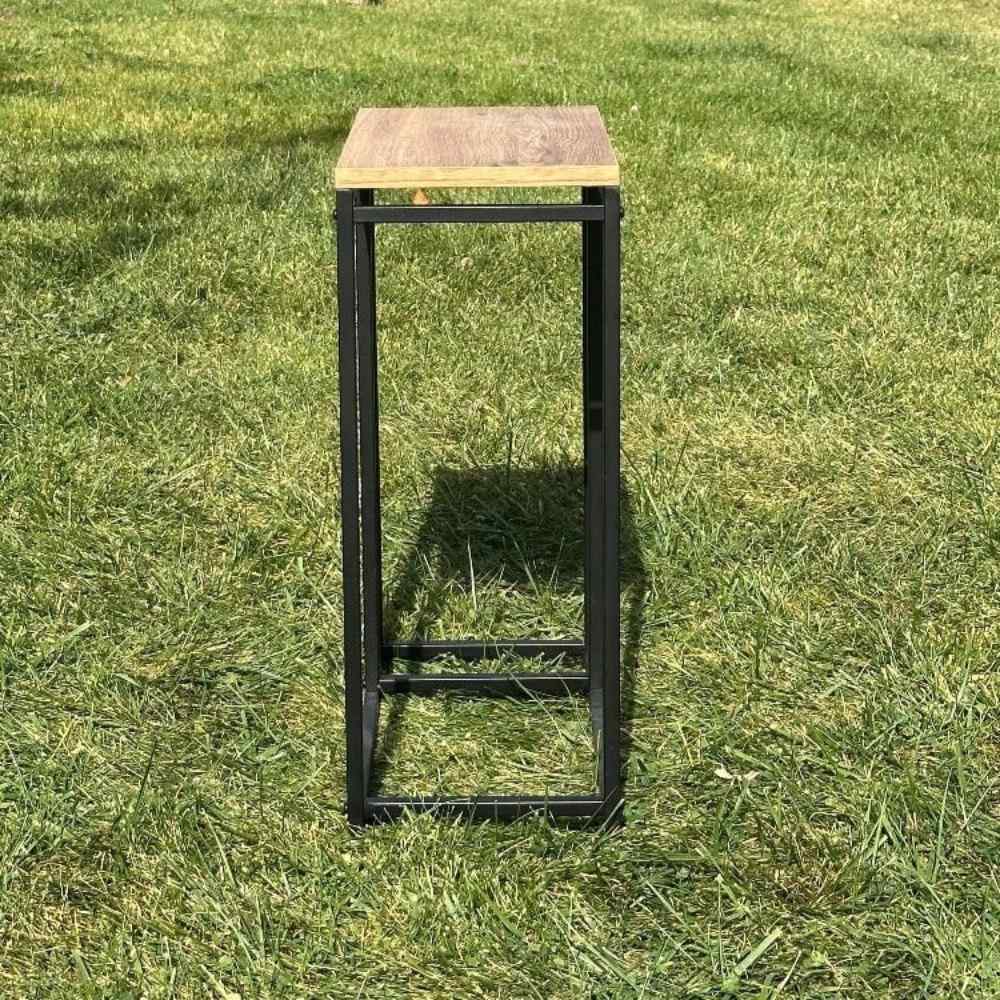 Side view of a minimalist black metal log rack with a wooden top, placed outdoors on grass, highlighting its narrow depth and contemporary style