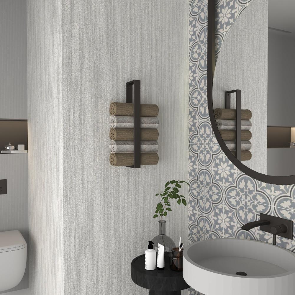A bathroom featuring a minimalist vertical towel rack in matte black holding neatly rolled towels, mounted beside a round mirror with patterned tiles, creating a stylish and functional design.