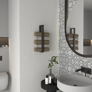 A bathroom featuring a minimalist vertical towel rack in matte black holding neatly rolled towels, mounted beside a round mirror with patterned tiles, creating a stylish and functional design.