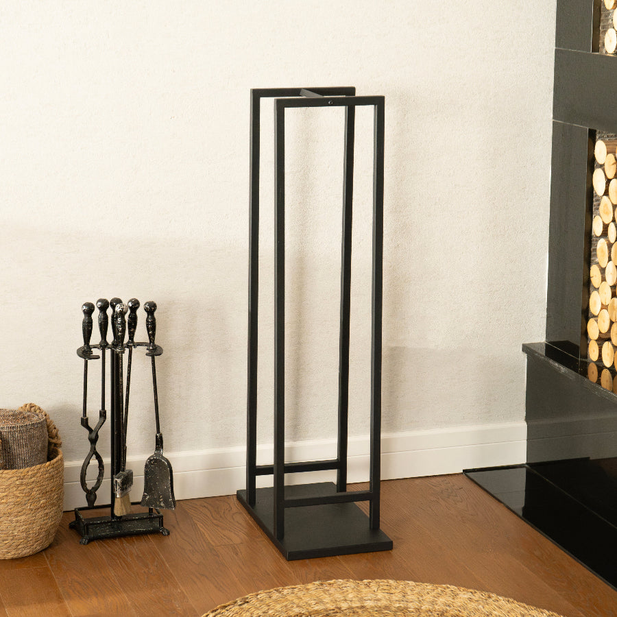Black metal firewood holder in front of a fireplace with tools and a basket.
