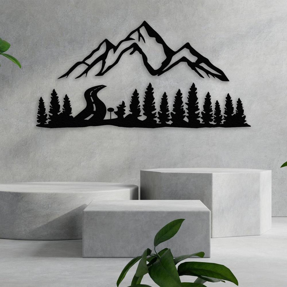 Black metal wall art featuring a scenic mountain range and dense pine forest, with a winding road leading through the trees, mounted on a neutral concrete backdrop for a modern, nature-inspired decor theme.