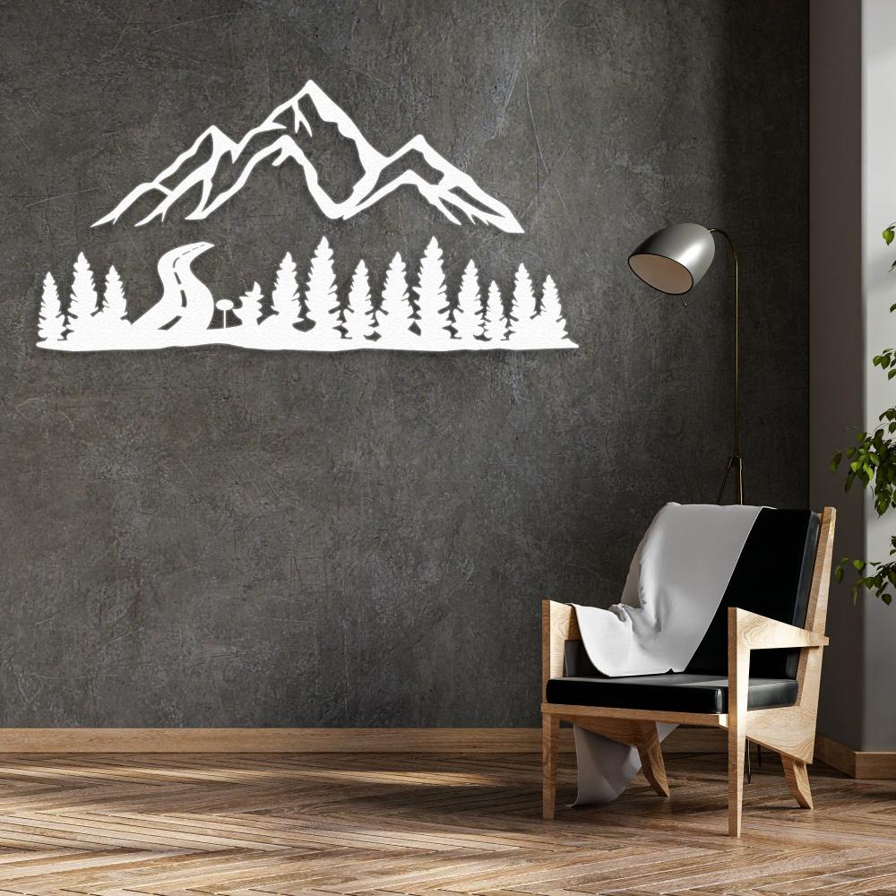 White mountain and forest-themed metal wall art decor mounted on a textured gray wall, paired with a modern wooden armchair draped in a soft blanket, creating a sophisticated and cozy living space.